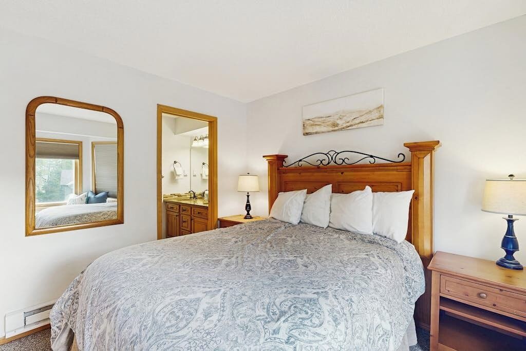 A bedroom with a bed, a nightstand, a mirror, and a wall-mounted artwork.