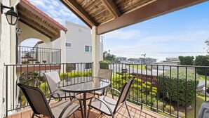 A covered balcony with a round table and chairs, a pergola, and a view of a residential area. - Classic getaway by the sea within walking distance to everything w/ocean views (Cayucos)