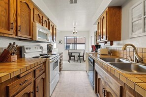 A kitchen with wooden cabinets, a microwave, stove, sink, and a dining area with chairs.