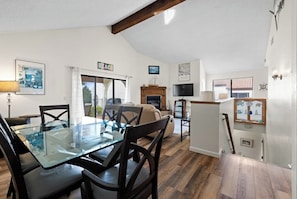 A dining area with a glass table and chairs, a fireplace, a television, and a view of the outdoors. - Classic getaway by the sea within walking distance to everything w/ocean views (Cayucos)