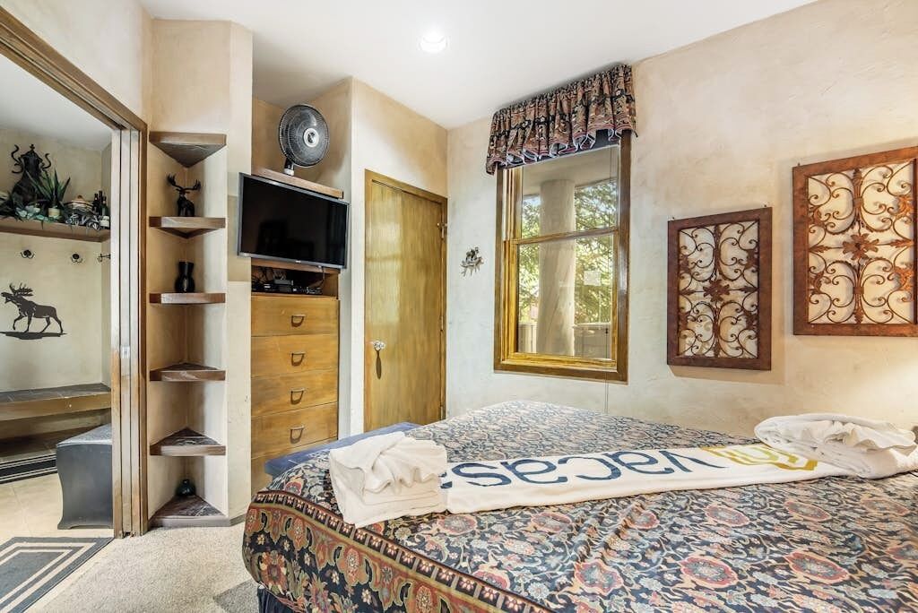 Un dormitorio con cama, televisor, armario y ventana con cortinas.