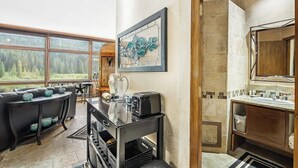 Eine moderne Küche mit einem großen Fenster, ein Essbereich mit einem schwarzen Tisch und Stühlen sowie ein Badezimmer mit einem Holzwaschtisch.