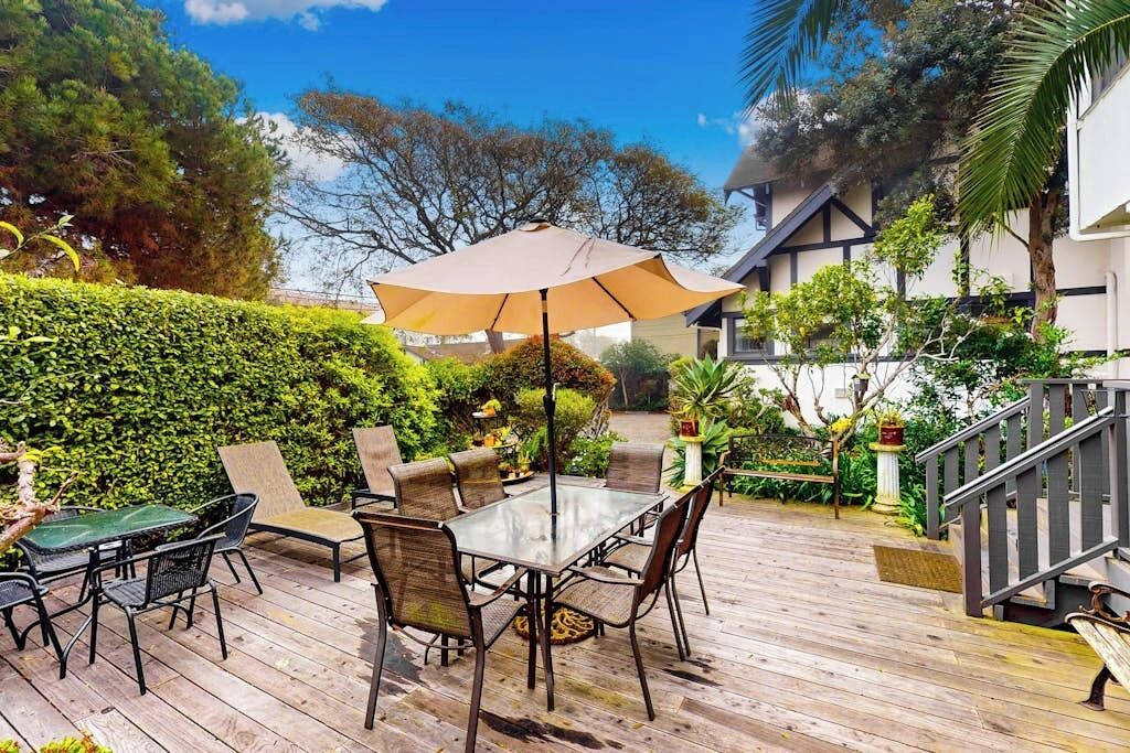 An outdoor patio with a table and chairs, surrounded by greenery and a staircase.