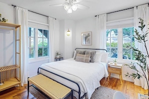 Ein Schlafzimmer mit einem Bett, Nachttischen, einer Bank und einem Fenster mit Vorhängen.