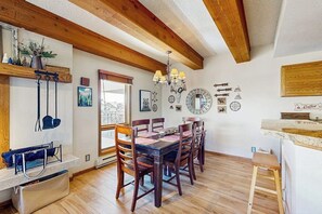Un espace repas agrémenté de poutres en bois, d’un lustre et offrant une vue sur l’extérieur.