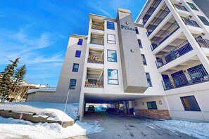 Un immeuble à plusieurs étages doté de balcons, d’un espace de stationnement et surplombant un ciel dégagé.