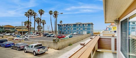 A hotel with a balcony overlooking a parking lot and a beach.