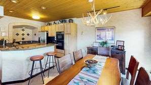 Una cocina con armarios de madera, una isla central con taburetes, una mesa de comedor con sillas y una araña.