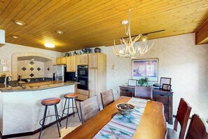 Eine Küche mit Holzausstattung, einer zentralen Kochinsel mit Barhocker, einem Esstisch mit Stühlen und einer Pendelleuchte.