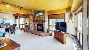 Un salón amplio con chimenea, techo de madera y ventanas grandes.