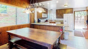 Une cuisine avec des meubles de rangement en bois, une table à manger en bois et des luminaires suspendus.