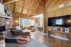 Ein großzügiger Wohnbereich mit Steinwand, Holzboden und einem großen Flachbildfernseher sowie einer gemütlichen Sitzecke.