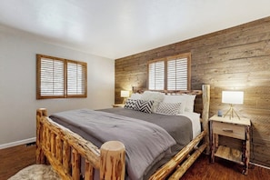 Ein Schlafzimmer mit Holz-Kopfteil, einem Bett mit grauer Bettwäsche, zwei Nachttischen mit Lampen und Holzwänden.