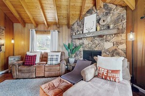 Ein gemütliches Wohnzimmer mit Kamin aus Stein, Ledersofas und einer Holzbalkendecke.