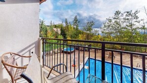 Un balcón con piscina, mobiliario exterior y vistas a árboles y colinas.