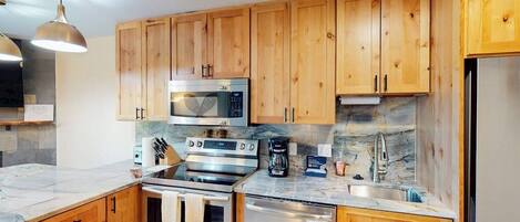 A kitchen with wooden cabinets, stainless steel appliances, and a marble countertop.