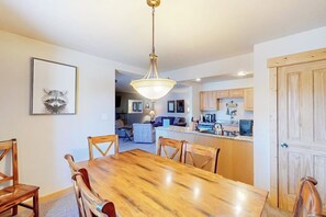 A dining area with a wooden table and chairs, a pendant light, and a framed picture on the wall. - Mountain view condo with hot tub, walk to Snowflake Lift & Main Street (Breckenridge)