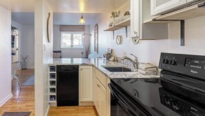 Una cocina con armarios blancos, estufa negra y una ventana.
