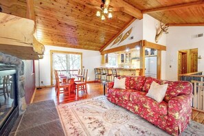Ein rustikales Interieur mit Kamin aus Stein, Holzbalkendecke, einem roten blumigen Sofa und einem Essbereich mit Holzkästen.