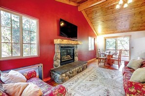 Ein Zimmer mit Kamin aus Stein, einem darüber montierten Fernseher, einer roten Wand und einem großen Fenster.