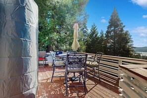 Une terrasse extérieure avec une table et des chaises, un parasol et une vue sur les arbres et les collines.