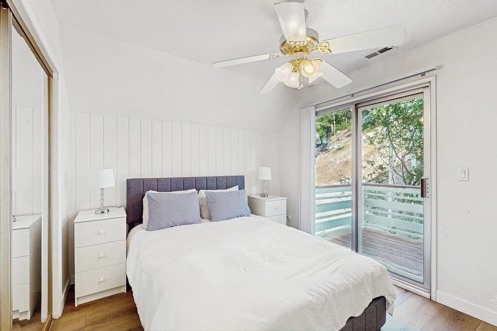 Ein Schlafzimmer mit Bett, Nachttischen, Deckenventilator und einer Schiebetür zu einem Balkon.