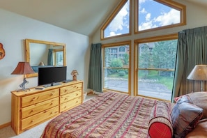 Ein Schlafzimmer mit einem großen Bett, einem Schminktisch, einem Fernseher und einem Fenster mit Vorhängen.