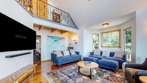 Ein großzügiges Wohnzimmer mit einem großen Flachbildfernseher, zwei blauen Sofas, einem Holztisch und einem gemusterten Teppich.