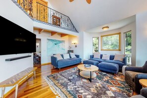 Ein großzügiges Wohnzimmer mit einem großen Flachbildfernseher, zwei blauen Sofas, einem Holztisch und einem gemusterten Teppich.