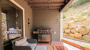 Une terrasse extérieure avec un barbecue, des meubles en osier et un mur en pierre.
