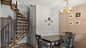Un coin repas avec une table et des chaises en bois, un escalier en colimaçon et des décorations murales sur le thème des animaux.