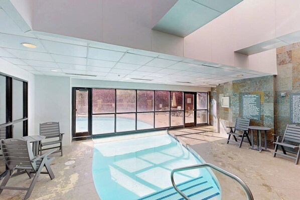 An indoor swimming pool with clear glass walls, a tiled floor, and several lounge chairs and tables. - Efficient Mountain Escape W/ Murphy Bed, Shared Pool, Slope Access & Kitchenette (Crested Butte)