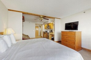 A bedroom with a bed, a TV, a wooden dresser, and a kitchen area visible through an open door. - Efficient Mountain Escape W/ Murphy Bed, Shared Pool, Slope Access & Kitchenette (Crested Butte)