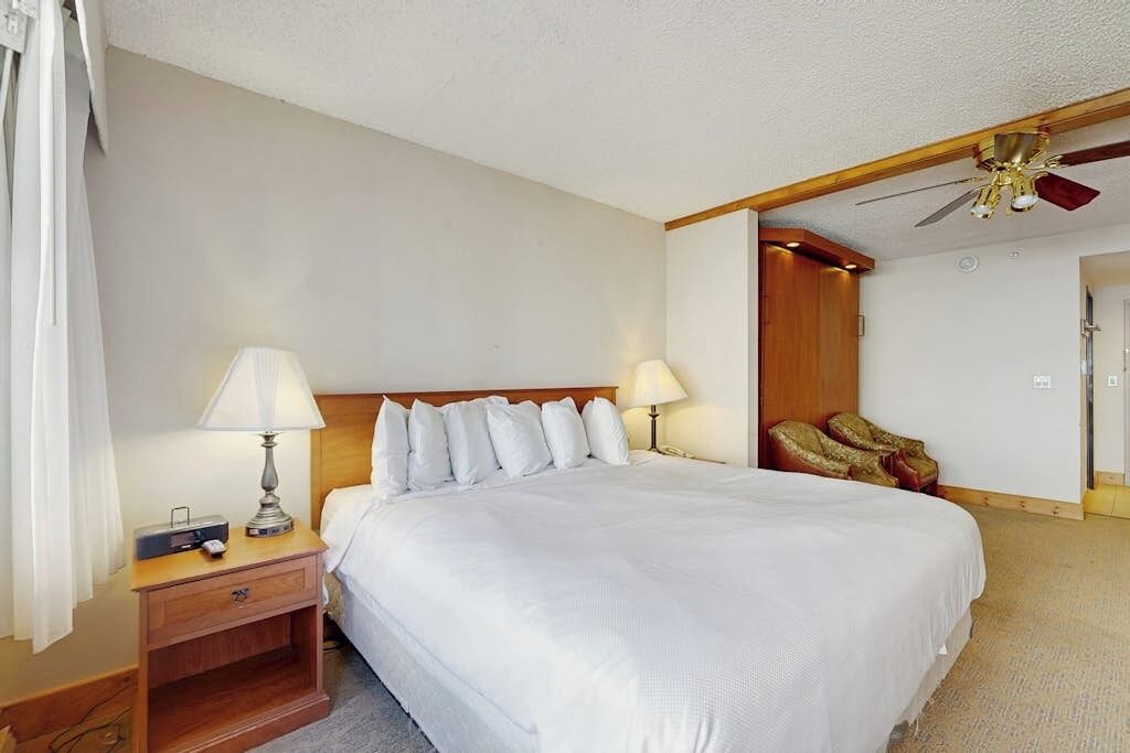 Een hotelkamer met een groot bed, twee bedlampen, een houten hoofdbord, een nachtkastje met een radio en een plafondventilator.