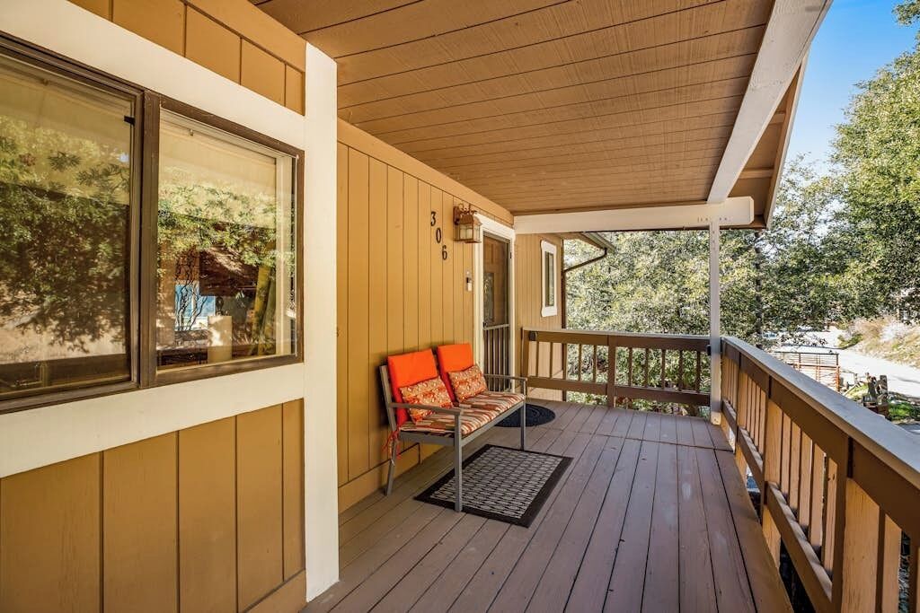 A wooden deck with a bench and a door leading to a covered area.