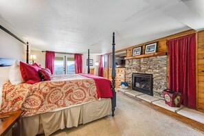Ein Schlafzimmer mit einem Bett, einem Kamin aus Stein und Blick ins Freie.