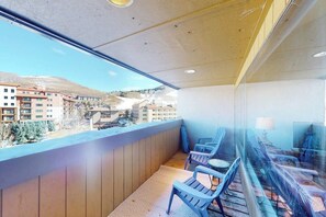 Ein Balkon mit Blick auf Gebäude und Berge, mit Holzboden und blauen Stühlen.