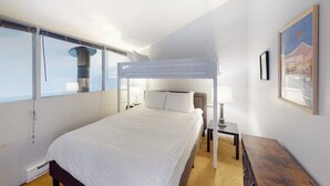 Un dormitorio con una litera, una mesita de noche con lámpara, una mesita auxiliar y un cuadro en la pared.
