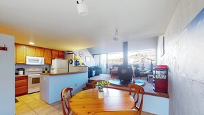 Una cocina con armarios de madera, un microondas y una estufa. Hay un comedor con mesa y sillas de madera.