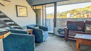 Una sala de estar con una escalera, un sillón azul, un sofá de cuero marrón y vistas a un pueblo de montaña.