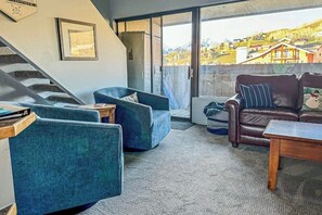 Ein Wohnzimmer mit Treppe, einem blauen Sessel, einem braunen Ledersofa und Blick auf eine Bergstadt.