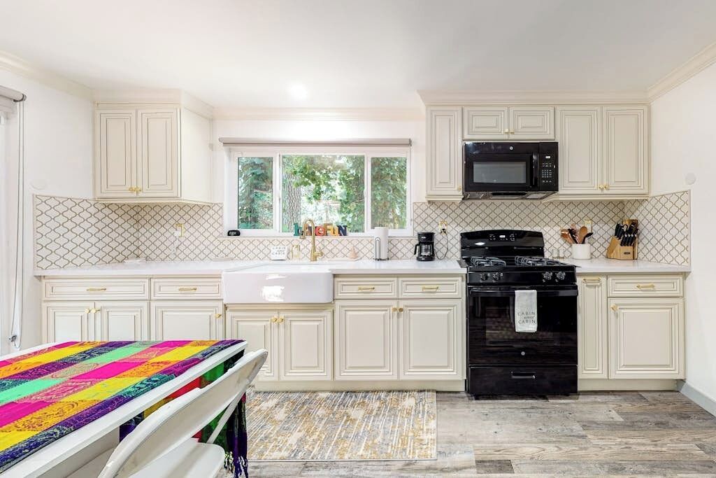 A kitchen with white cabinetry, a black stove, a microwave, and a window with greenery outside.