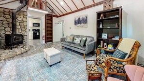 Een gezellige woonkamer met een stenen openhaard, een bank, een gestreept fauteuil en een boekenkast.