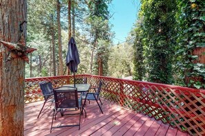 A wooden deck with a table and chairs, surrounded by a red lattice fence and dense greenery. - Forest-view cabin with deck, grill, wood stove, washer/dryer, & fast WiFi (Crestline)