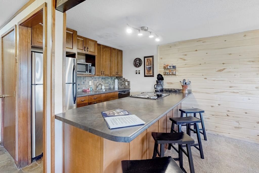 A kitchen with wooden cabinets, stainless steel appliances, a bar area, and a small island with stools.