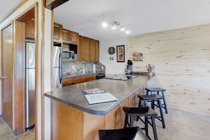 A kitchen with wooden cabinets, stainless steel appliances, a bar area, and a small island with stools. - Beautiful mountain home steps to ski slopes with fireplace (Durango)
