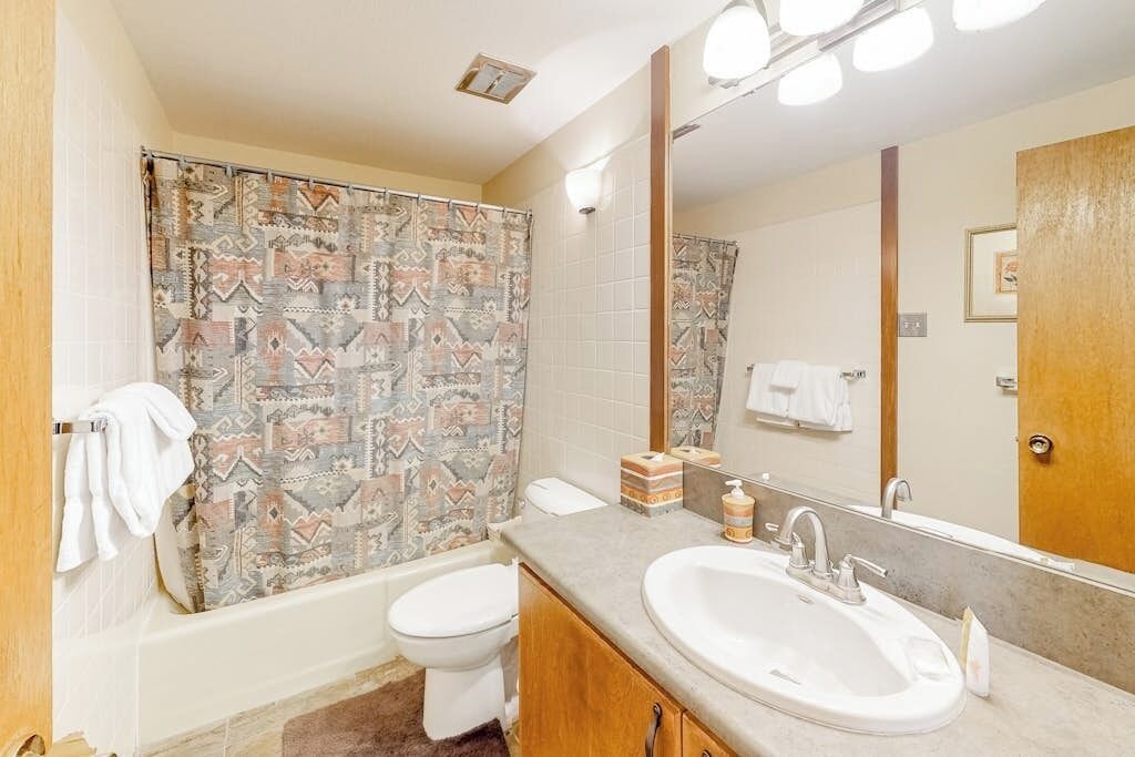 Une salle de bain équipée d’un rideau de douche, de toilettes, d’un lavabo et d’un miroir.