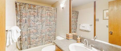 Une salle de bain équipée d’un rideau de douche, de toilettes, d’un lavabo et d’un miroir.