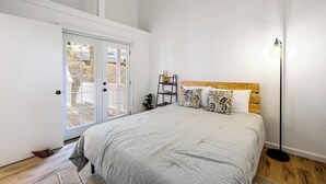 A bedroom with a bed, a nightstand, a floor lamp, and a door leading to an outdoor area. - Dog-friendly Arrowhead Villas cottage with deck, fireplace & W/D- great locale (Lake Arrowhead)