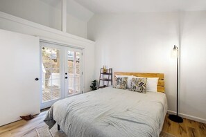 Ein Schlafzimmer mit Bett, Nachttisch, Stehlampe und einer Tür, die zu einem Außenbereich führt.